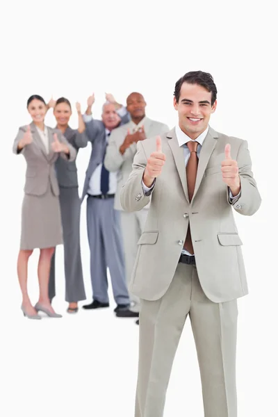 親指をあきらめて彼の背後にあるチームとビジネスマンの笑みを浮かべてください。 — ストック写真