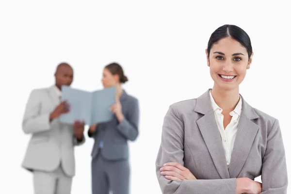 Smiling saleswoman with arms crossed and colleagues behind her — Stock Photo, Image