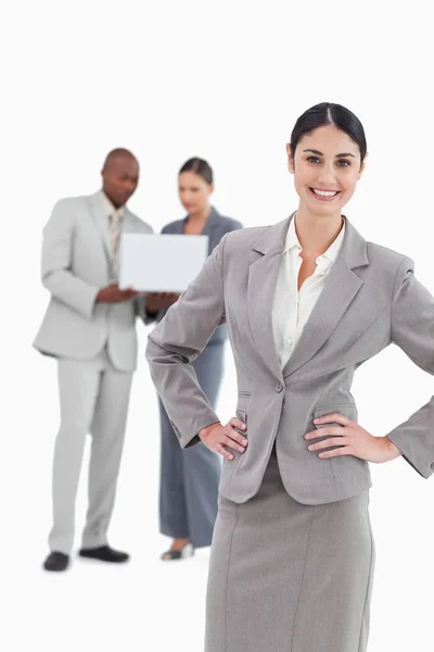 Smiling businesswoman with hands on her hip and colleagues behin — Stock Photo, Image