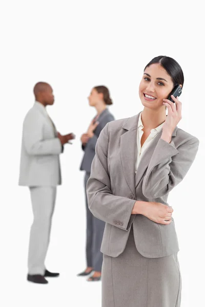 Smiling saleswoman with cellphone and colleagues behind her — Stock Photo, Image