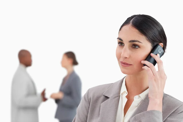 Saleswoman with cellphone and colleagues behind her — Stock Photo, Image