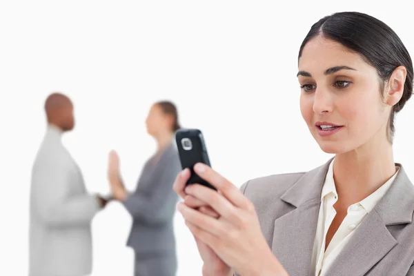 Businesswoman looking at cellphone with colleagues behind her — Stock Photo, Image