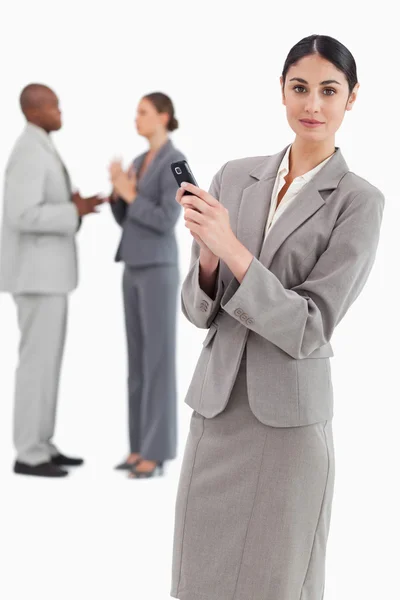 Продавець тримає мобільний телефон з колегами позаду неї — стокове фото