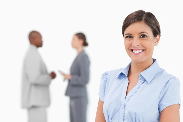 Smiling businesswoman with talking associates behind her — Stock Photo, Image