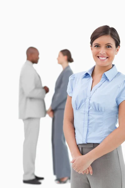 Smiling businesswoman with talking co-workers behind her — Stock Photo, Image
