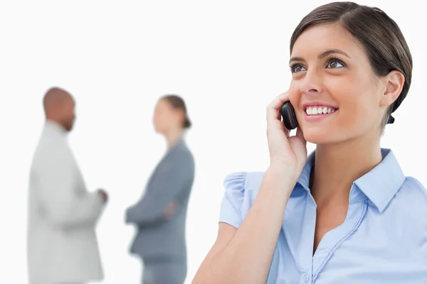 Lächelnde Geschäftsfrau mit Handy und Mitarbeitern hinter ihm — Stockfoto