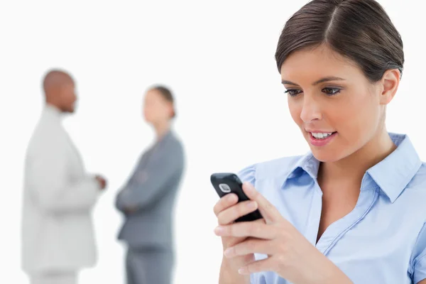 Geschäftsfrau liest SMS mit Mitarbeitern hinter sich — Stockfoto