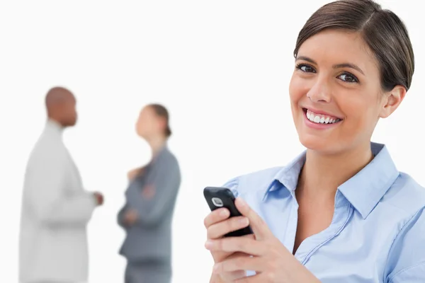 Smiling saleswoman with mobile phone and associates behind her — Stock Photo, Image