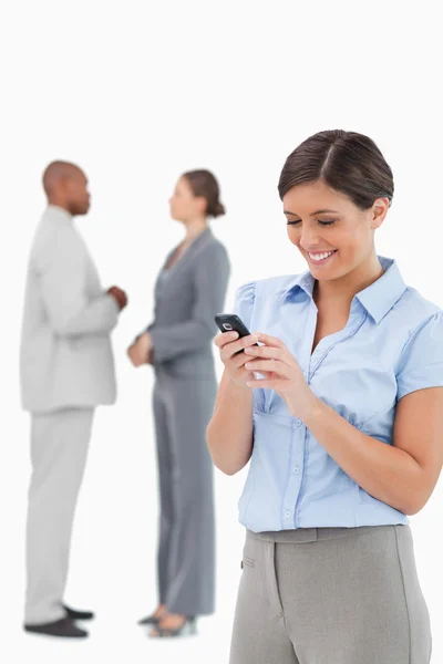 Businesswoman looking at cellphone with associates behind her — Stock Photo, Image