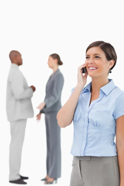 Glimlachend verkoopster op de telefoon met collega's achter haar — Stockfoto