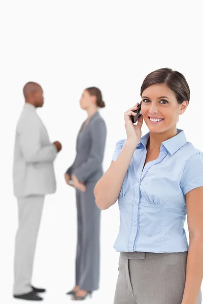 Smiling saleswoman on the phone with associates behind her — Stock Photo, Image