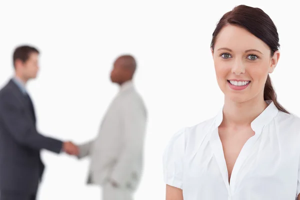 Smiling saleswoman with hands shaking trading partners behind he — Stock Photo, Image