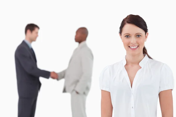 Empresária sorridente com mão apertando parceiros comerciais atrás — Fotografia de Stock