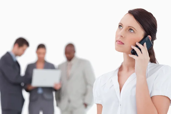 Businesswoman listening to caller with colleagues behind her — Stock Photo, Image