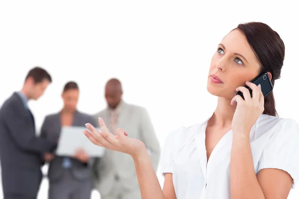 Tradeswoman talking on the phone with colleagues behind her — Stock Photo, Image