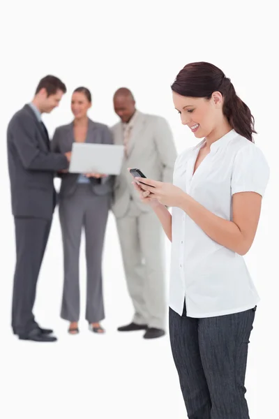 Saleswoman with mobile phone and colleagues behind her — Stock Photo, Image