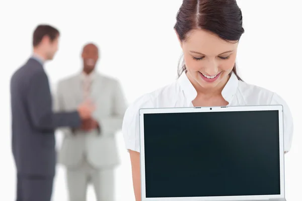 Деловая женщина показывает ноутбук с партнерами позади нее — стоковое фото