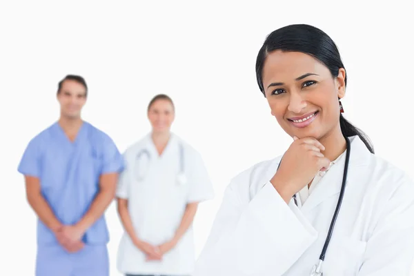 Uśmiechający się lekarza w pozie myślicieli z kolegami za nią — Zdjęcie stockowe