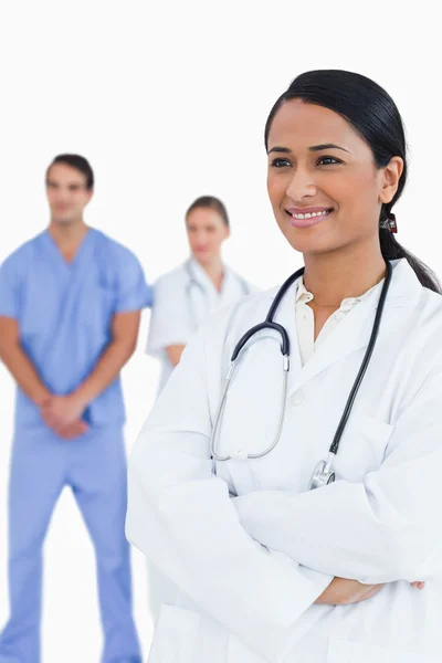 Médico sorridente com os braços dobrados e colegas atrás dela — Fotografia de Stock