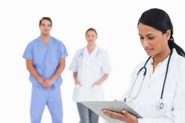Doctor taking notes with staff behind her — Stock Photo, Image
