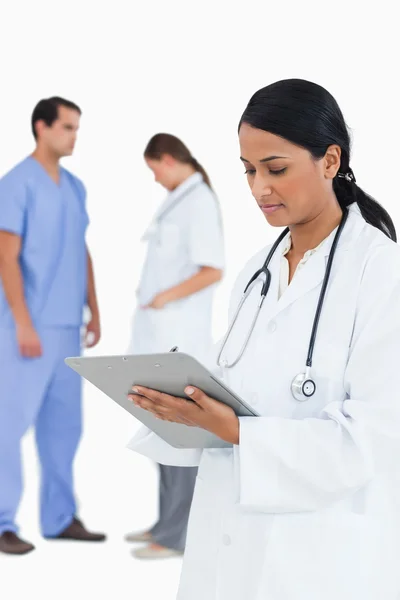Doctor taking notes with staff members behind her — Stock Photo, Image