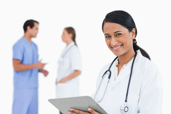 Uśmiechający się lekarz ze schowka i kolegów za nią — Zdjęcie stockowe