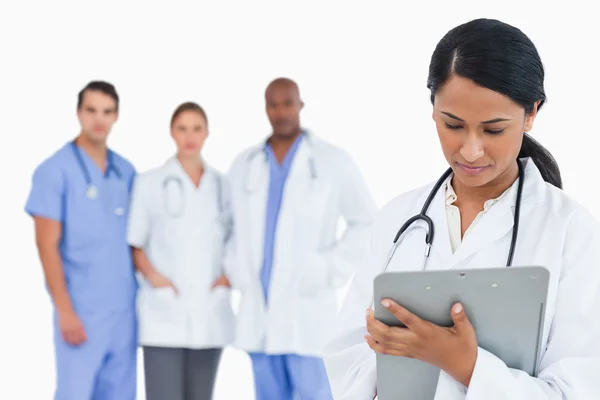 Female doctor taking notes on clipboard with staff members behin — Stock Photo, Image