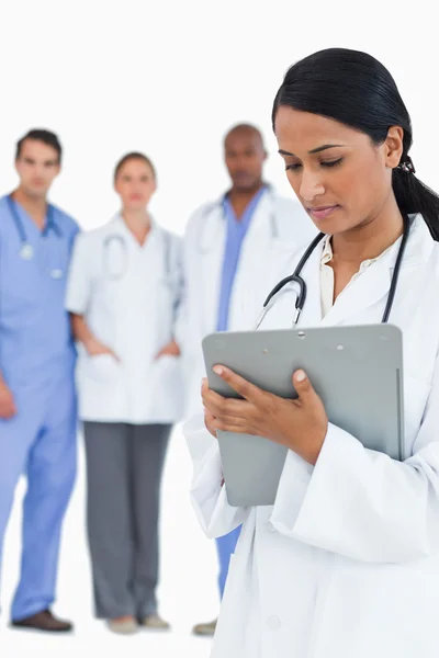 Female doctor reading notes with staff members behind her — Stock Photo, Image