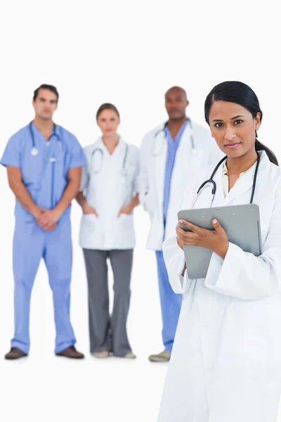 Female doctor with clipboard and colleagues behind her — Stock Photo, Image