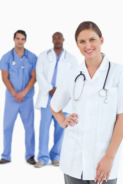 Médico sorridente com colegas masculinos por trás dela — Fotografia de Stock