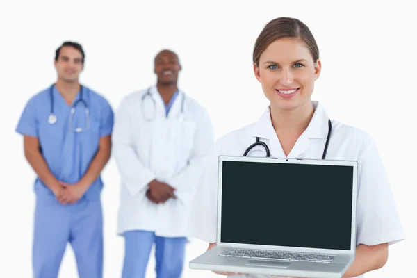 Médico sonriente mostrando cuaderno con colegas detrás de ella —  Fotos de Stock