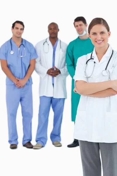 Uśmiechający się lekarz z założonymi rękami i kolegów za nią — Zdjęcie stockowe