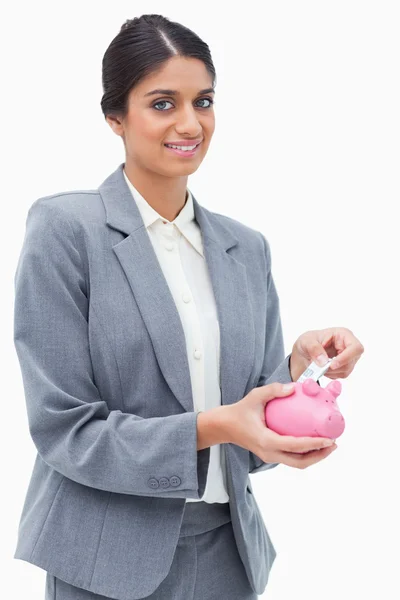 Assistente de banco sorrindo colocando dinheiro no banco porquinho — Fotografia de Stock