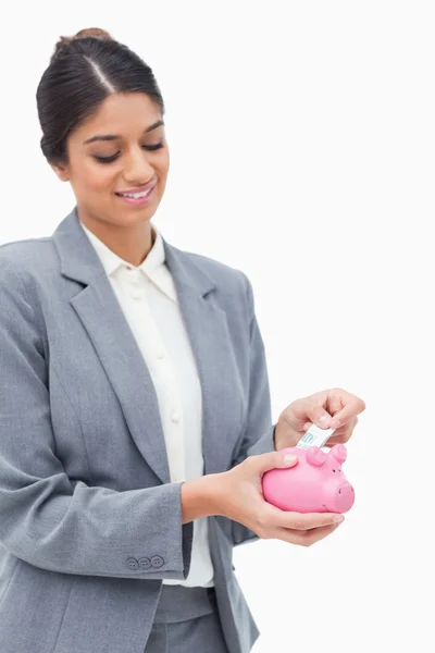 Assistente de banco sorrindo colocando nota bancária em banco porquinho — Fotografia de Stock