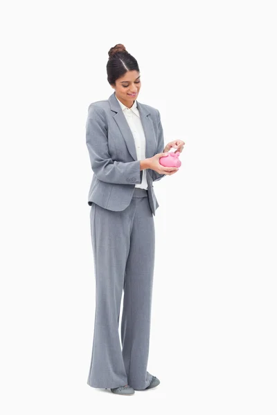 Smiling female banker putting bank note into piggy bank — Stock Photo, Image