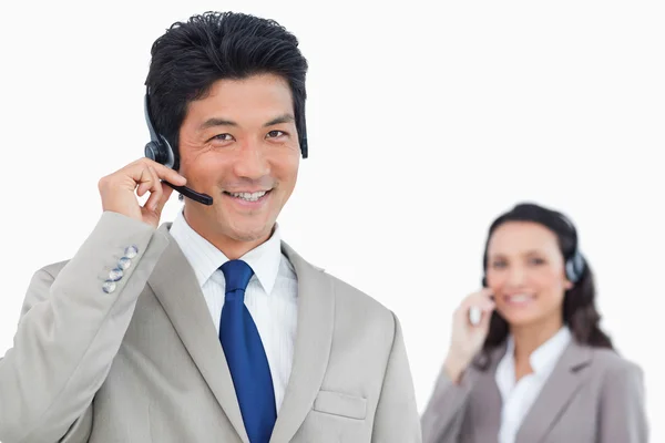 Call center agent met collega achter hem glimlachen — Stockfoto