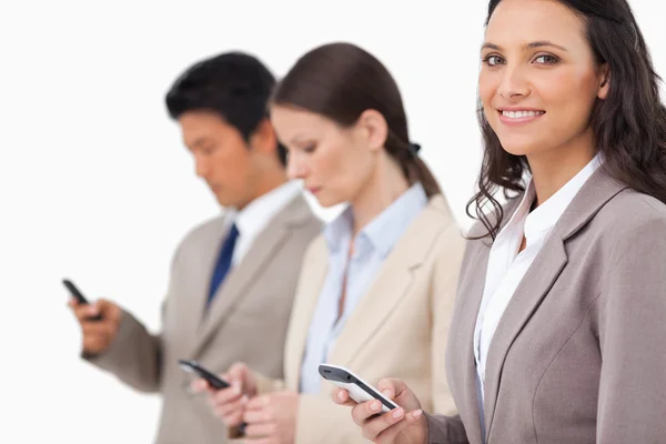 Smiling saleswoman with cellphone next to colleagues — Stock Photo, Image