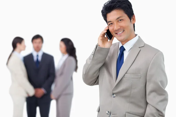 Biznesmen uśmiechający się na telefon i zespół za nim — Zdjęcie stockowe
