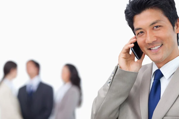 Hombre de negocios sonriente en el teléfono móvil y el equipo detrás de él —  Fotos de Stock