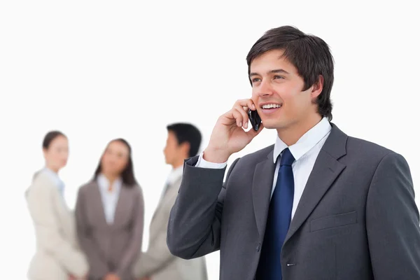 Salesman talking on cellphone with colleagues behind him — Stock Photo, Image