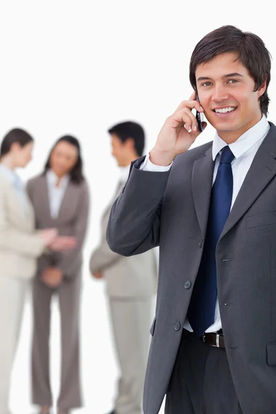 Smiling salesman on cellphone with team behind him — Stock Photo, Image