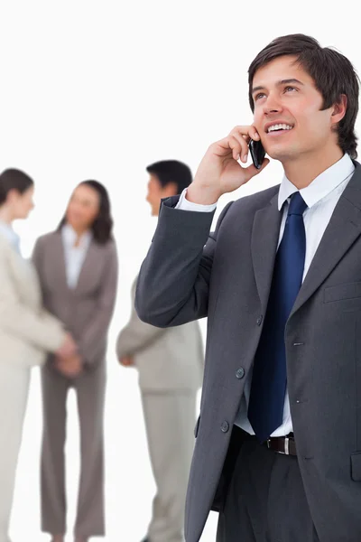 Salesman talking on mobile phone with team behind him — Stock Photo, Image
