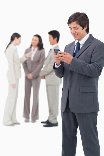 Leende försäljare håller mobiltelefon med teamet bakom honom — Stockfoto