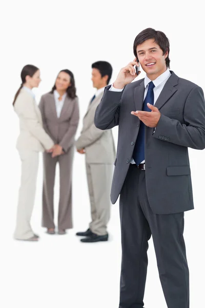 Vendedor falando no celular com a equipe atrás dele — Fotografia de Stock