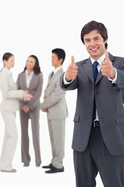 Salesman giving thumbs up with team behind him — Stock Photo, Image
