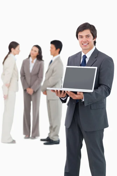 Vendedor sorridente mostrando tela de laptop com equipe atrás dele — Fotografia de Stock
