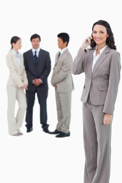 Smiling saleswoman on her cellphone with team behind her — Stock Photo, Image