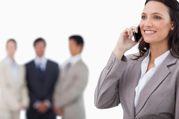 Smiling saleswoman on her mobile phone with team behind her — Stock Photo, Image