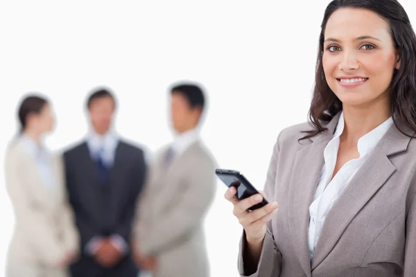 Smiling saleswoman holding cellphone with team behind her — Stock Photo, Image