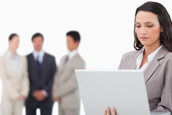 Saleswoman with laptop and colleagues behind her — Stock Photo, Image